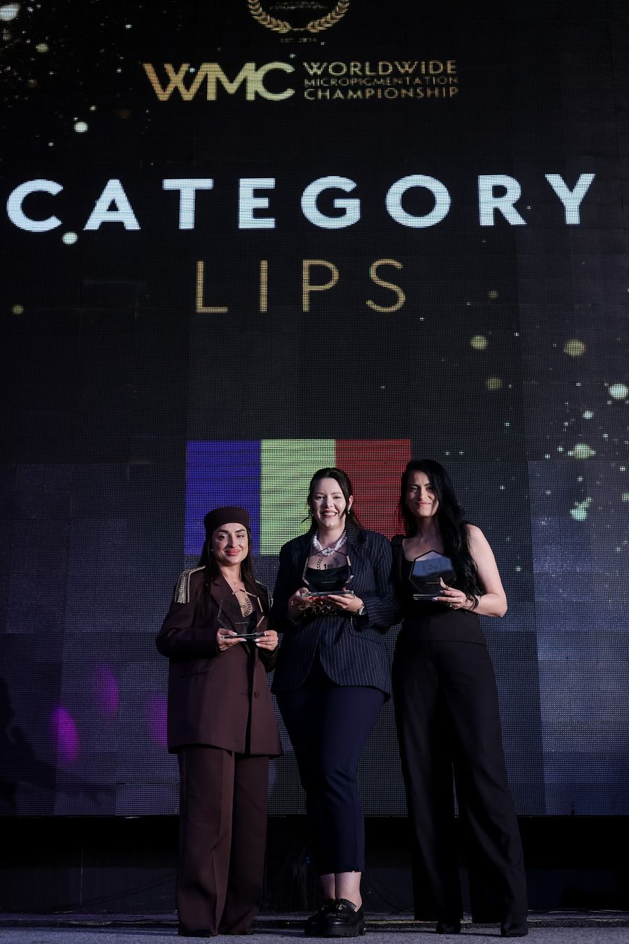 Trei artiste pe scenă, în categoria Lips, cu trofeele în mână și tricolorul pe ecranul din spate