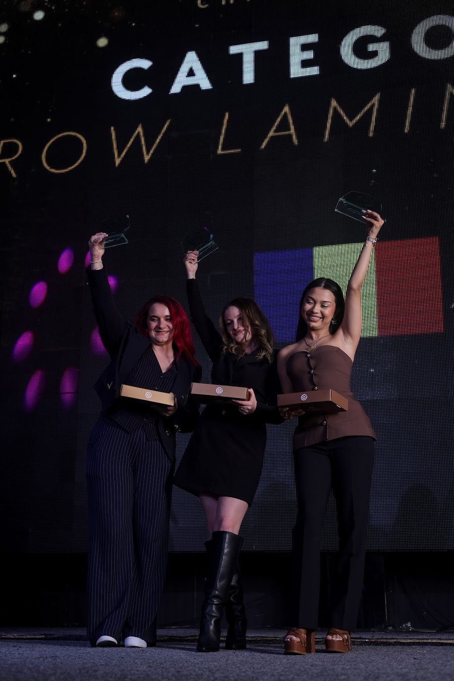 Trei artiste care ridică trofeele deasupra capului, cu tricolorul pe ecranul din spate
